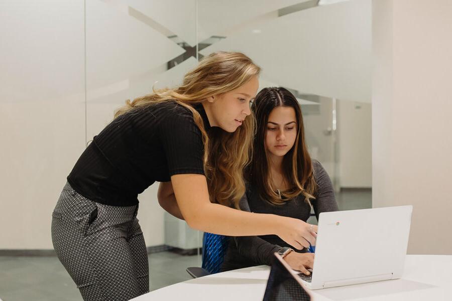 two students look at a computer screen in the library